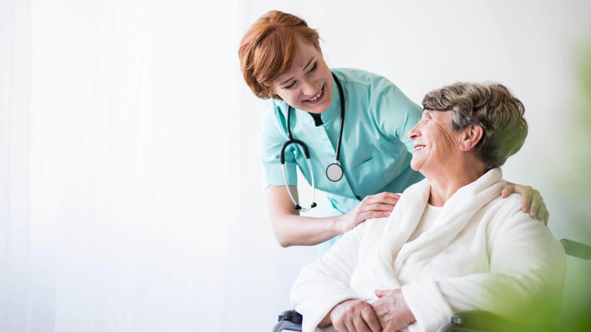 Eine Ärztin legt den Arm auf die Schulter einer Patientin. Dabei lächeln beide.
